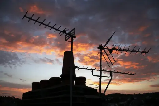 Silhouette of antennas and chimney against a sunset with orange, pink, and blue hues.