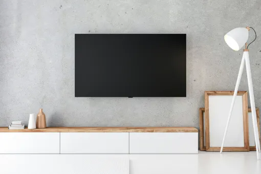 Living room with digital display showing time, weather, and schedule. Tablet on table; couch and plant in background.