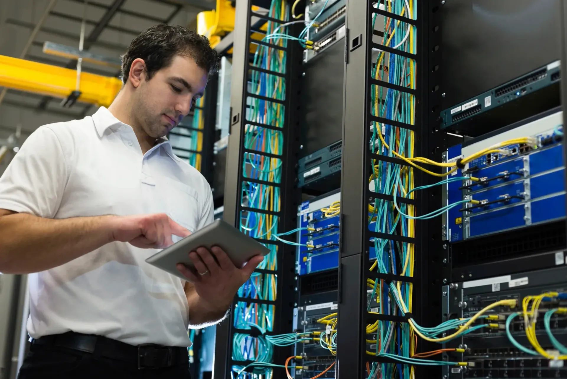 Man in server room using a tablet to check network equipment.