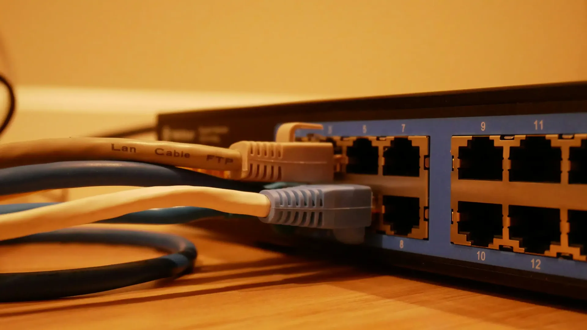 Ethernet switch with network cables plugged in, blue and beige cables, on a wood surface.