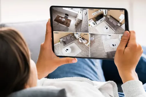 Person holding tablet displaying live feeds from several security cameras inside a home.
