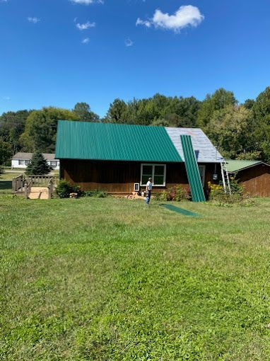 A house with a green roof is sitting in the middle of a grassy field.