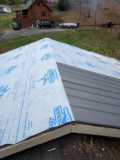 A roof with a lot of roofing material on it and a house in the background.
