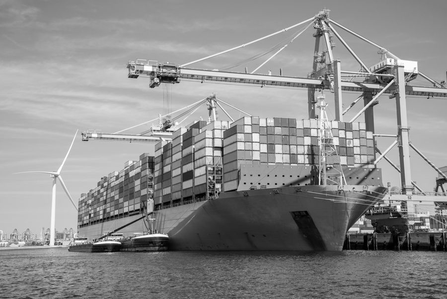Ein Schwarzweissfoto eines grossen Containerschiffs, das in einem Hafen vor Anker liegt.
