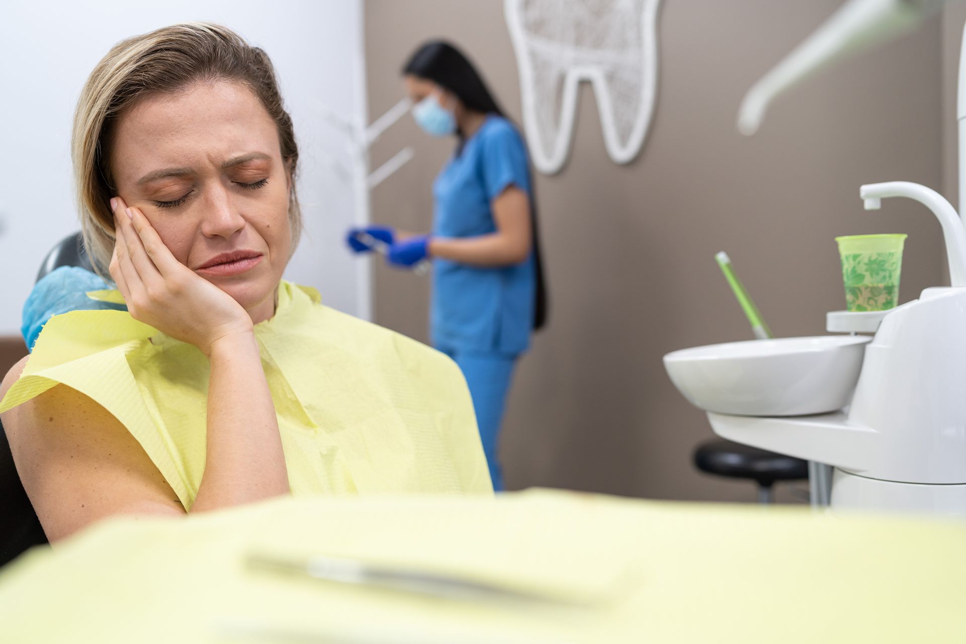 Woman in pain during emergency dental visit, sitting in dental chair holding cheek in discomfort.