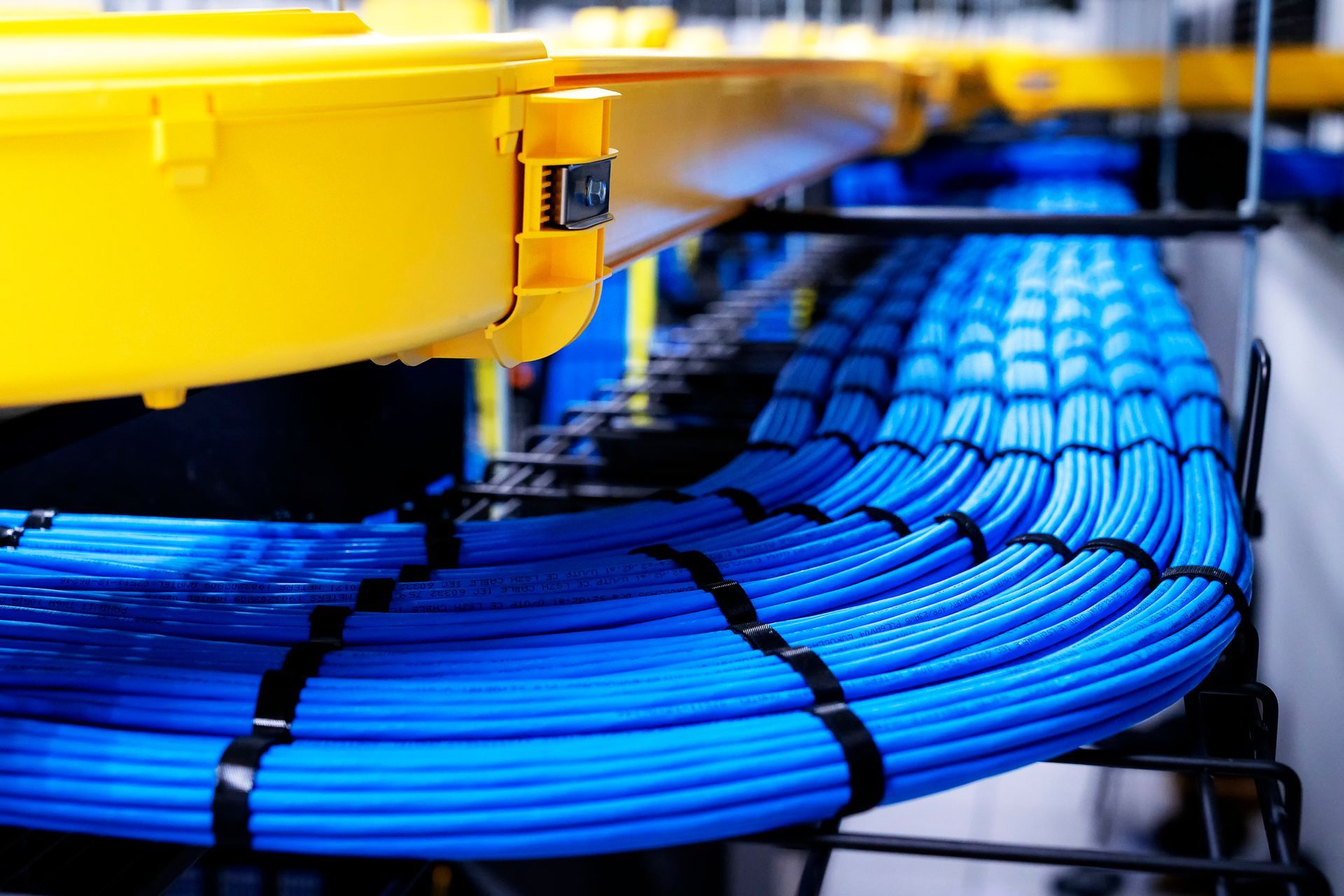 Blue network cables bundled on a black rack beneath a yellow overhead structure in a server room.