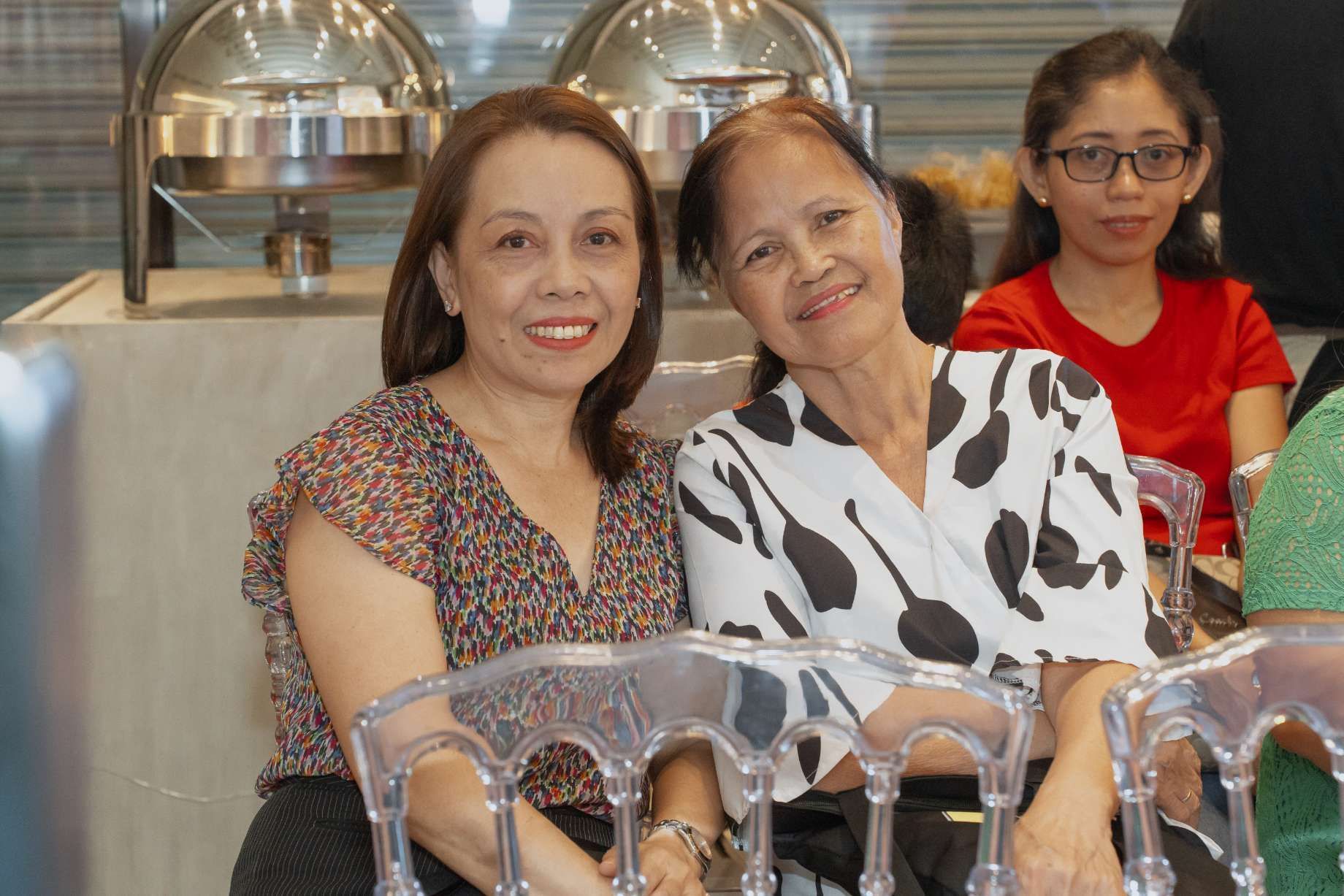 Two women are sitting next to each other in chairs and smiling for the camera.