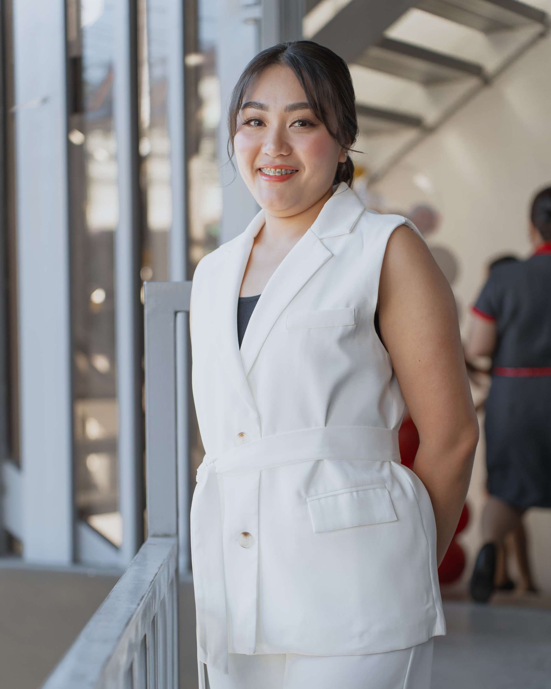 A woman in a white suit is standing in front of a window.