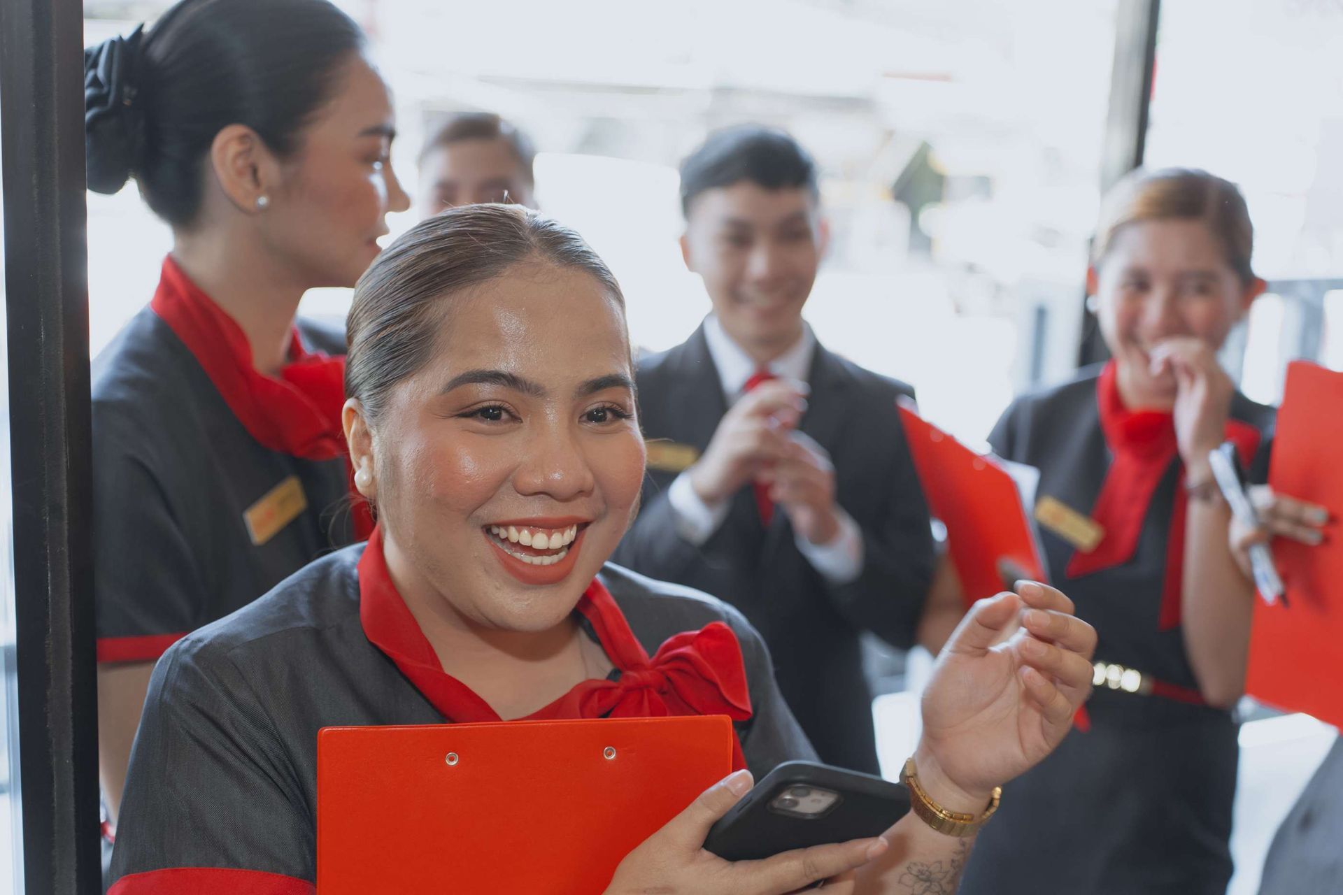 A woman is smiling while holding a clipboard and a cell phone.