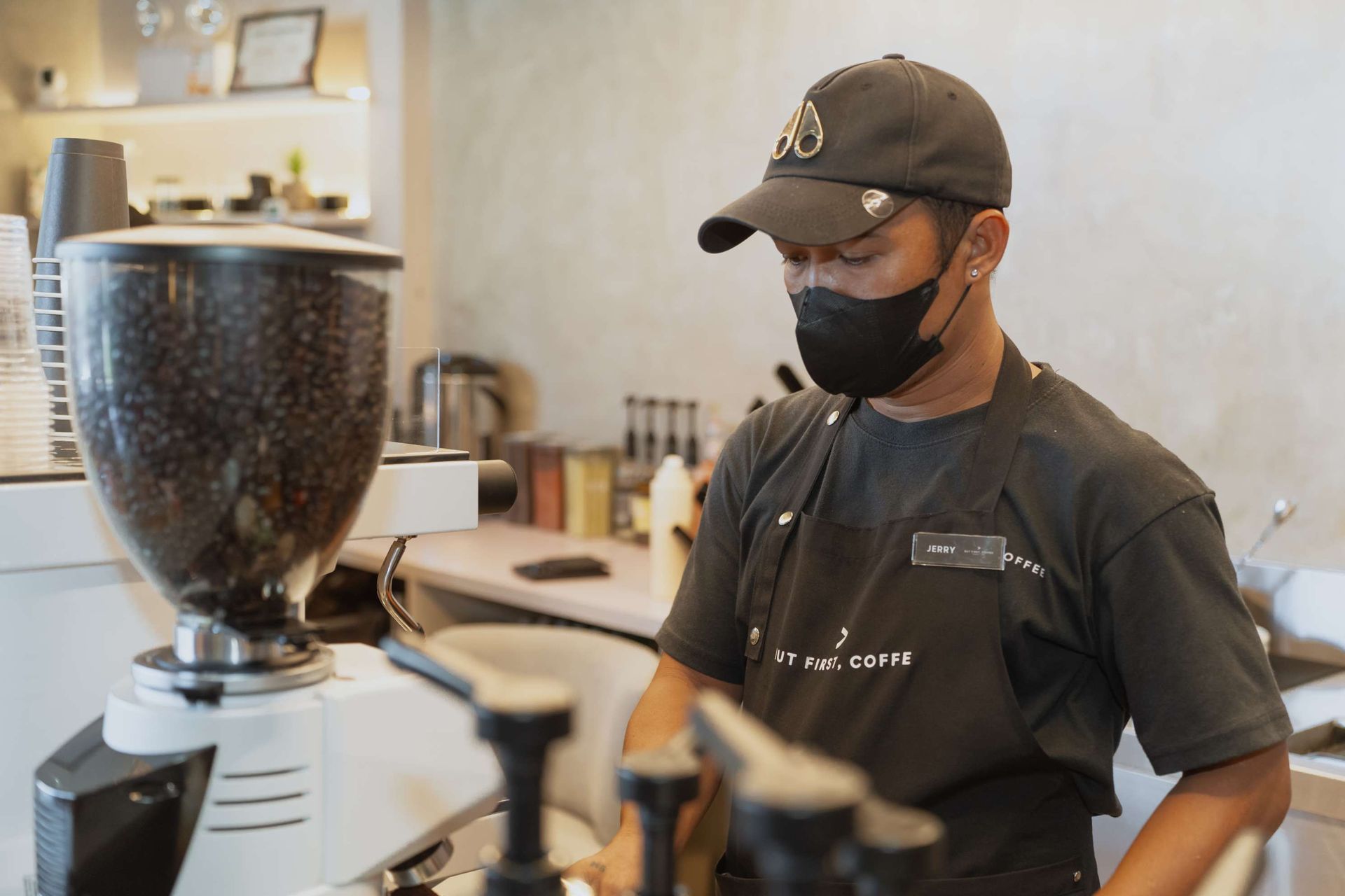 A man wearing a mask is making coffee in a coffee shop.