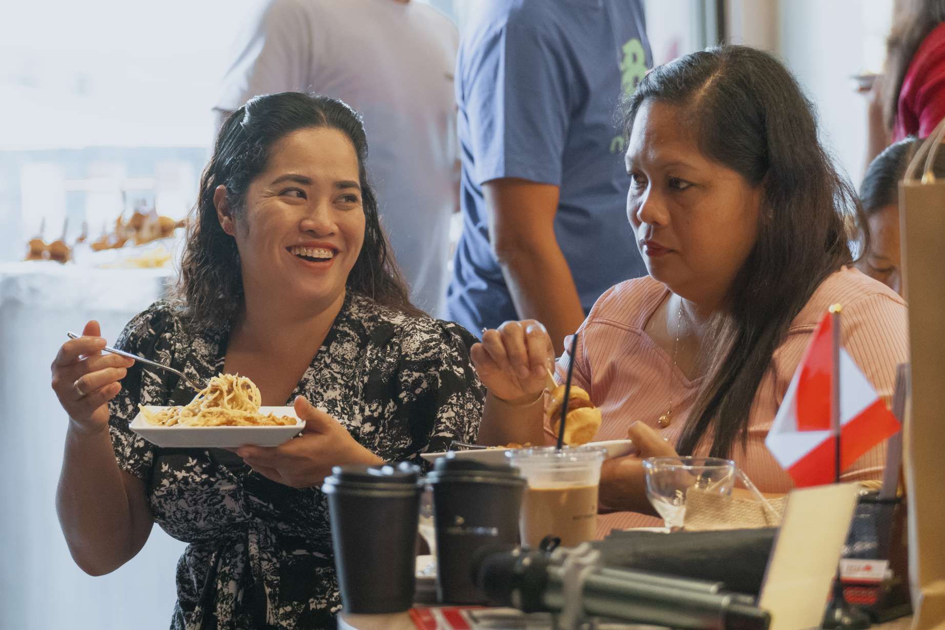 Two women are sitting at a table eating food and drinking coffee.