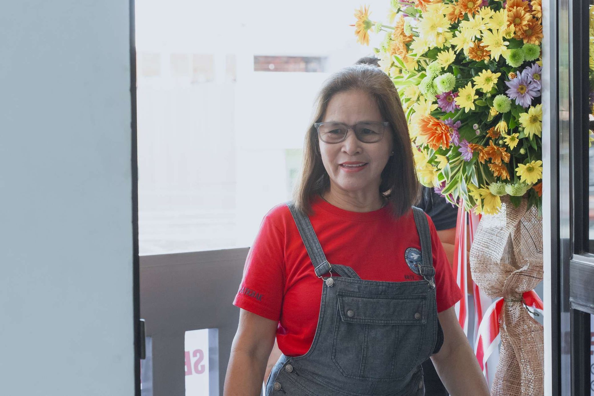 A woman wearing overalls and a red shirt is walking through a doorway.