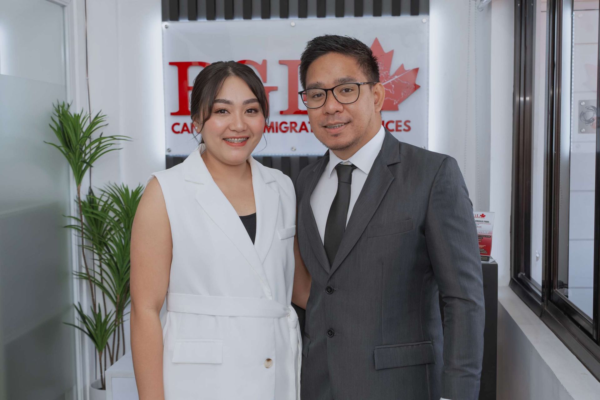 A man and a woman are posing for a picture in front of a window.