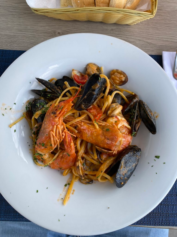 Un piatto di linguine ai frutti di mare con gamberi, cozze e vongole in salsa di pomodoro, con un cestino di pane accanto.
