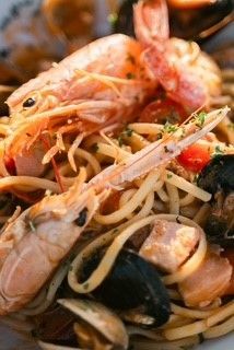 Primo piano di un piatto di pasta ai frutti di mare con gamberi, cozze, vongole e pesce a cubetti, servito in una salsa leggera.
