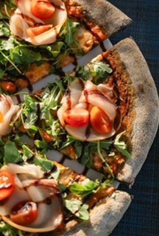 Vista dall'alto di una pizza a fette condita con rucola fresca, prosciutto a fette, pomodorini e un filo di glassa balsamica.