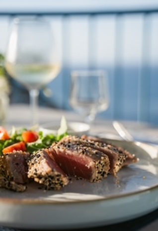 Fette di tonno scottato in crosta di sesamo servite su un piatto con un'insalata di contorno, con calici di vino sullo sfondo.