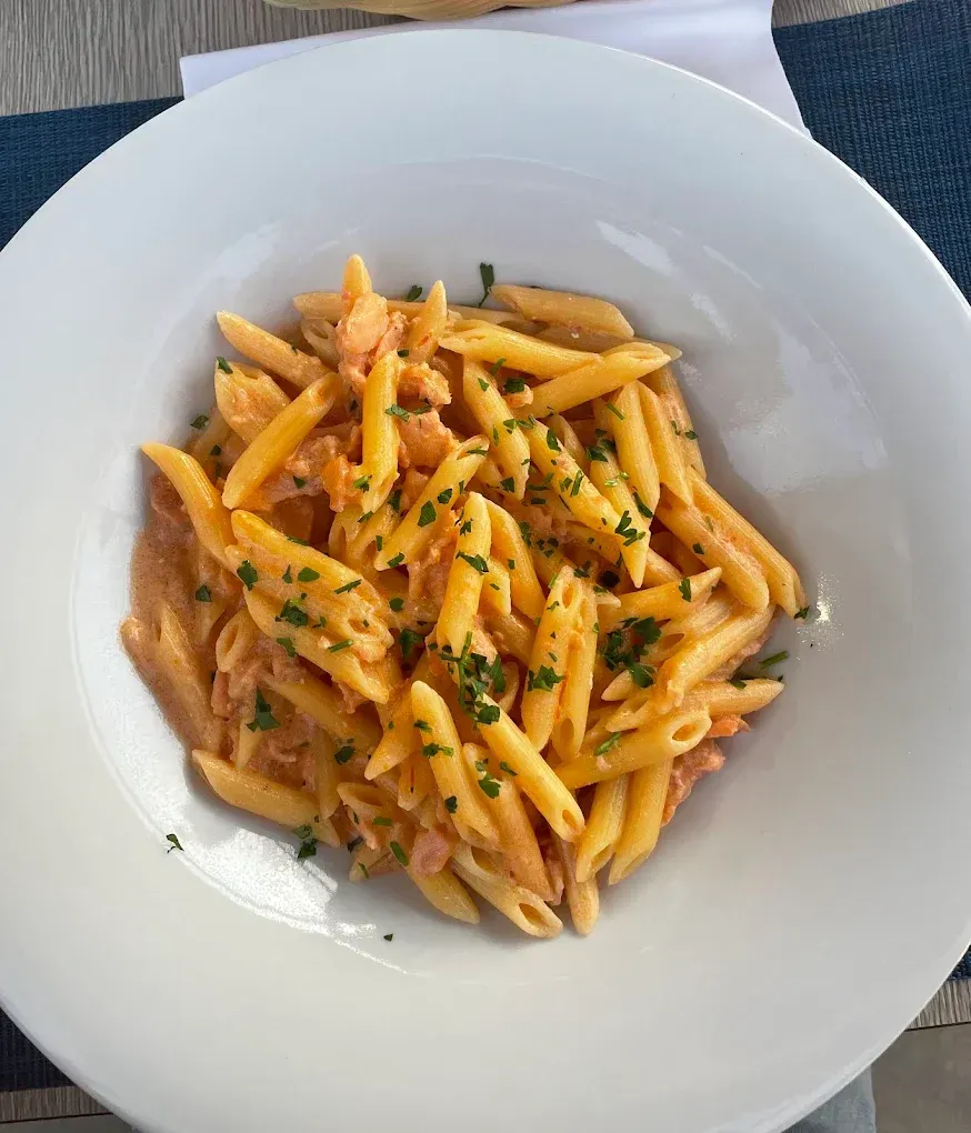Una ciotola bianca piena di penne condite con una cremosa salsa color salmone e guarnita con erbe aromatiche fresche.