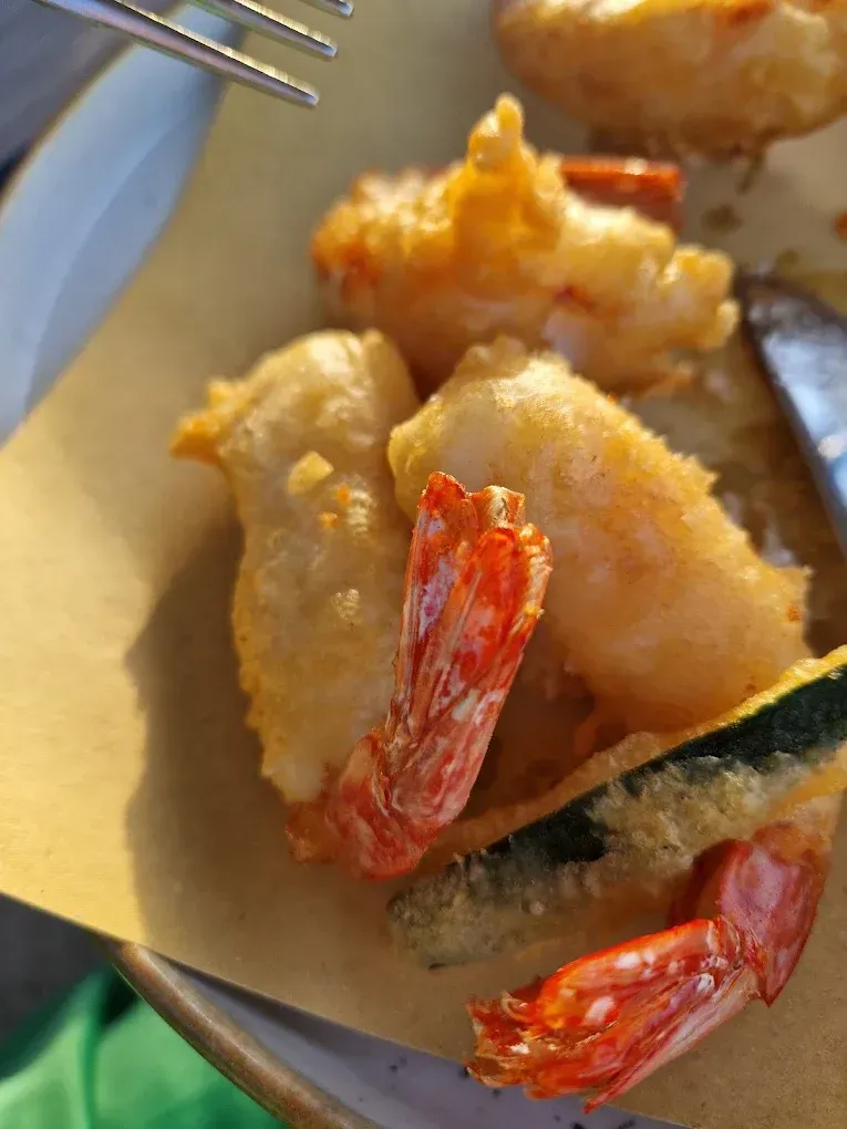 Gamberi fritti e una fetta di zucchina impanata su carta da forno, con una forchetta di metallo visibile in alto.