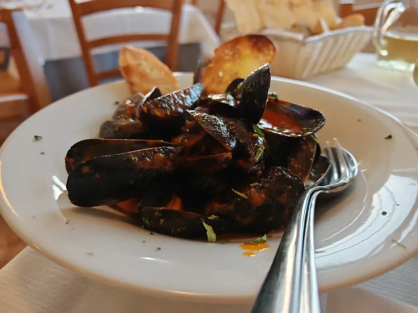 Un piatto di cozze in salsa di pomodoro con pane tostato, servito su un tavolo di ristorante.