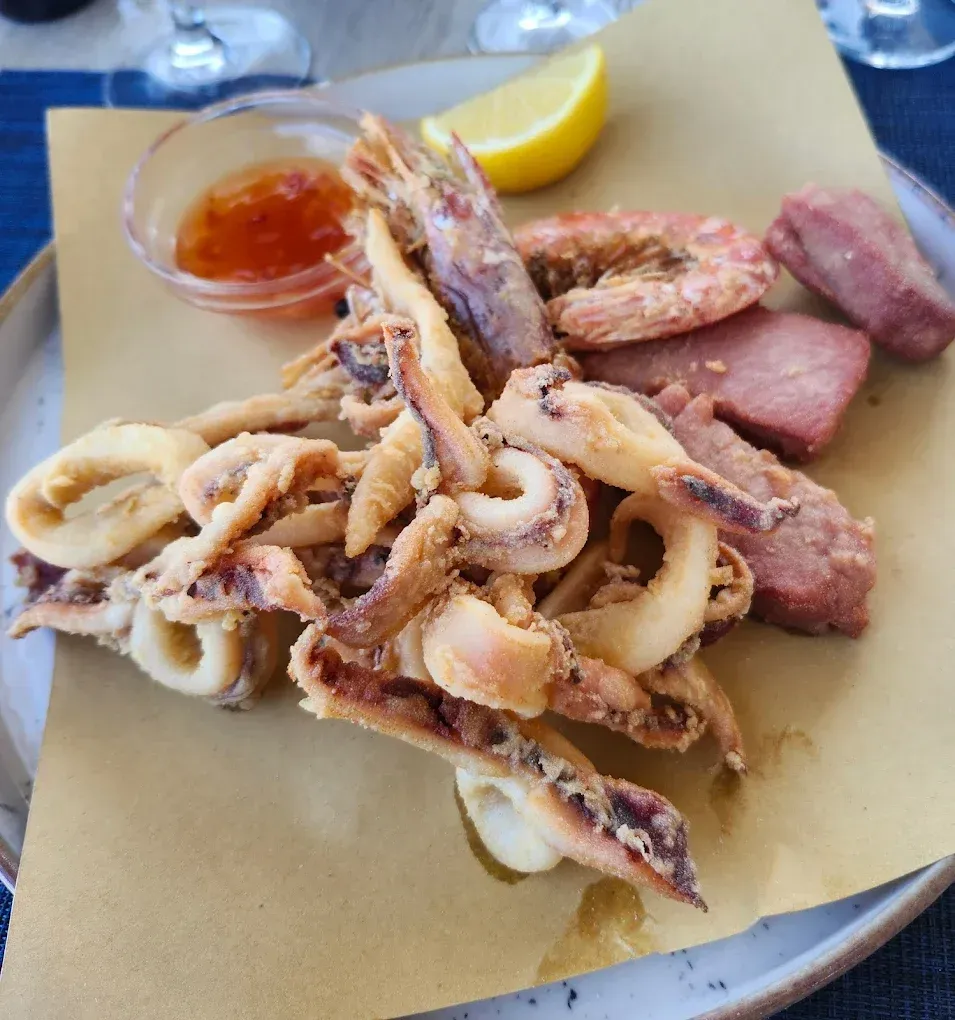 Una porzione di calamari e gamberi fritti con salsa d'accompagnamento e spicchi di limone su carta.