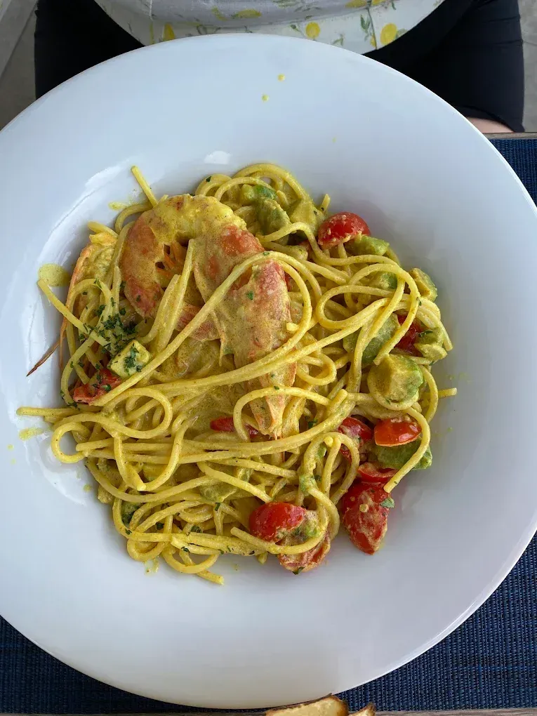 Un piatto di spaghetti con gamberi, pomodorini e avocado a cubetti in una salsa gialla e cremosa.