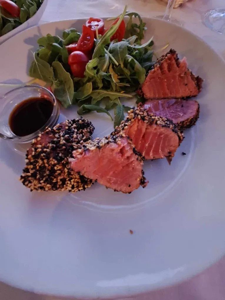 Fette di tonno scottate in crosta di sesamo, servite con un'insalata fresca di rucola e pomodorini e salsa di soia a parte.