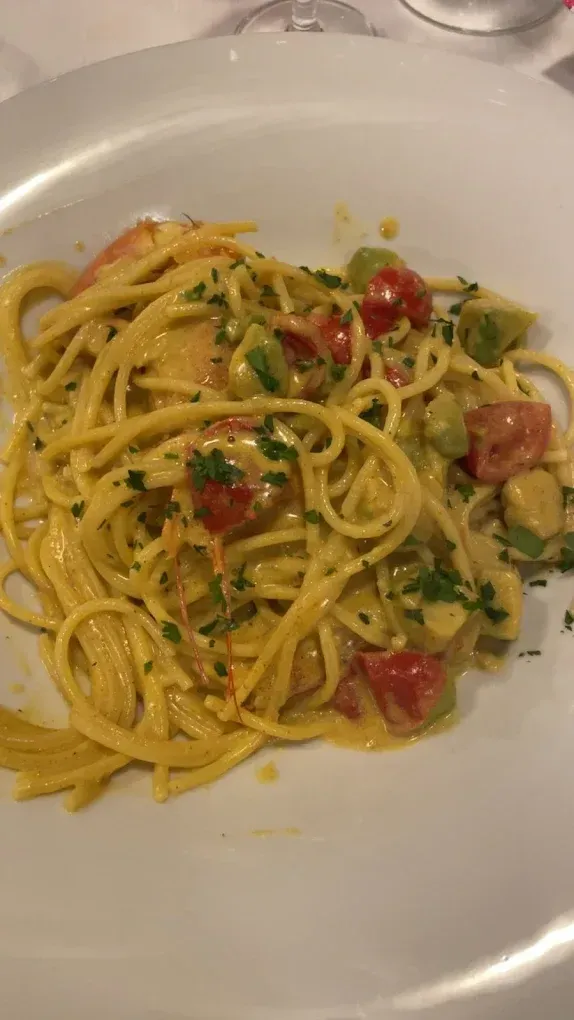 Un piatto di spaghetti conditi con una cremosa salsa giallo dorata, pomodori a cubetti ed erbe aromatiche fresche.