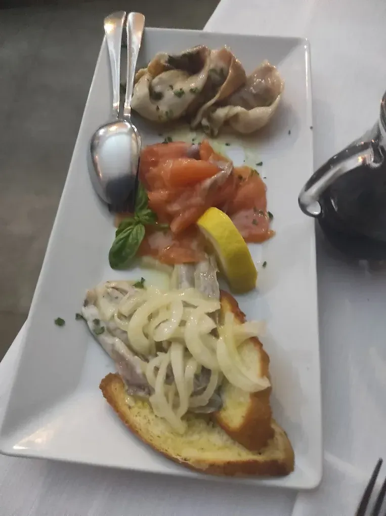 Un piatto rettangolare contenente tre antipasti: frutti di mare marinati, salmone affumicato al limone e basilico e pesce su crostini.