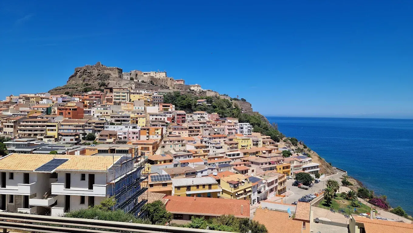 Una cittadina costiera con edifici raggruppati su una collina che si affaccia su un mare di un blu intenso sotto un cielo limpido.