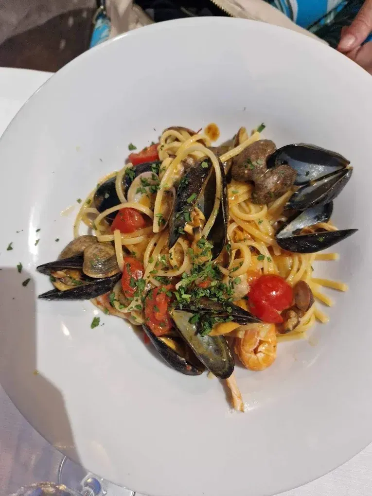 Un piatto bianco con linguine condite con cozze, pomodorini e erbe aromatiche fresche.