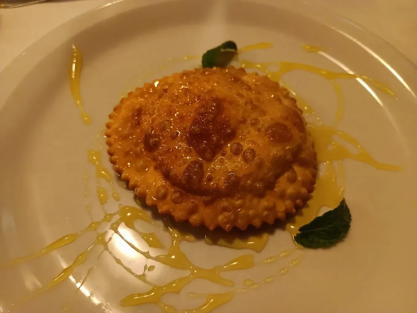 Una sfoglia di pasta fritta e ondulata, condita con salsa gialla e guarnita con foglie di menta, servita su un piatto bianco.