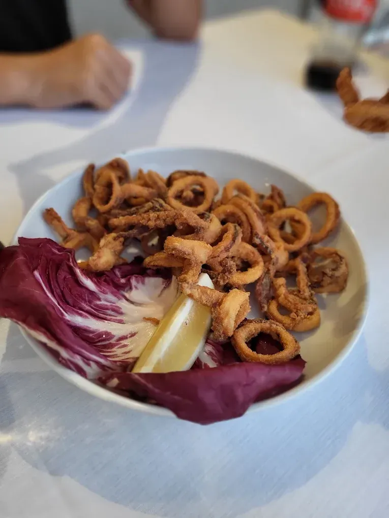 Una ciotola bianca piena di anelli di calamari fritti dorati, serviti su un letto di foglie di radicchio con uno spicchio di limone.