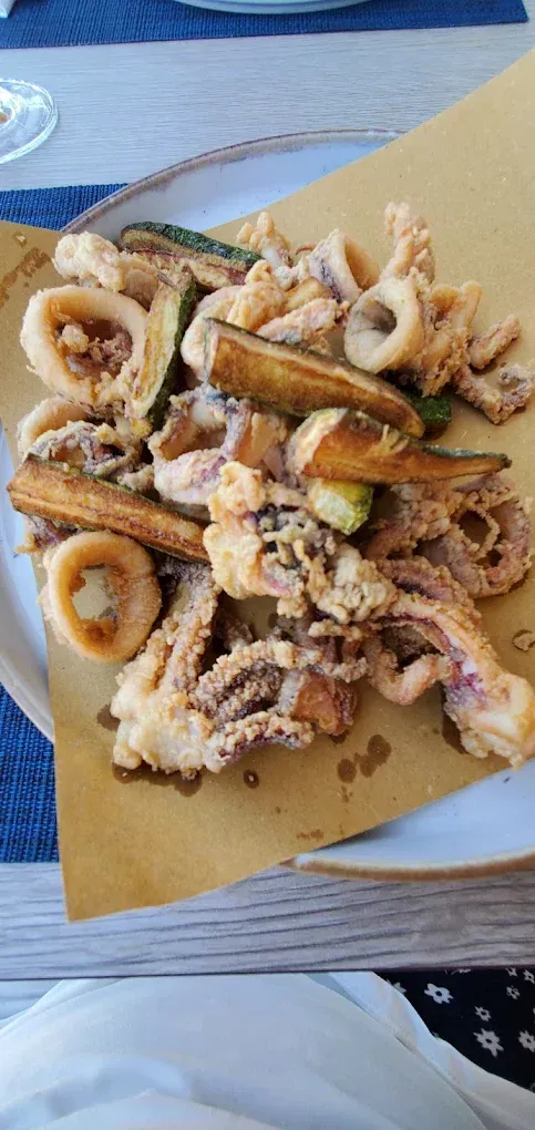 Un piatto misto di frutti di mare e verdure fritte, con anelli di calamari croccanti e bastoncini di zucchine, servito su carta marrone.