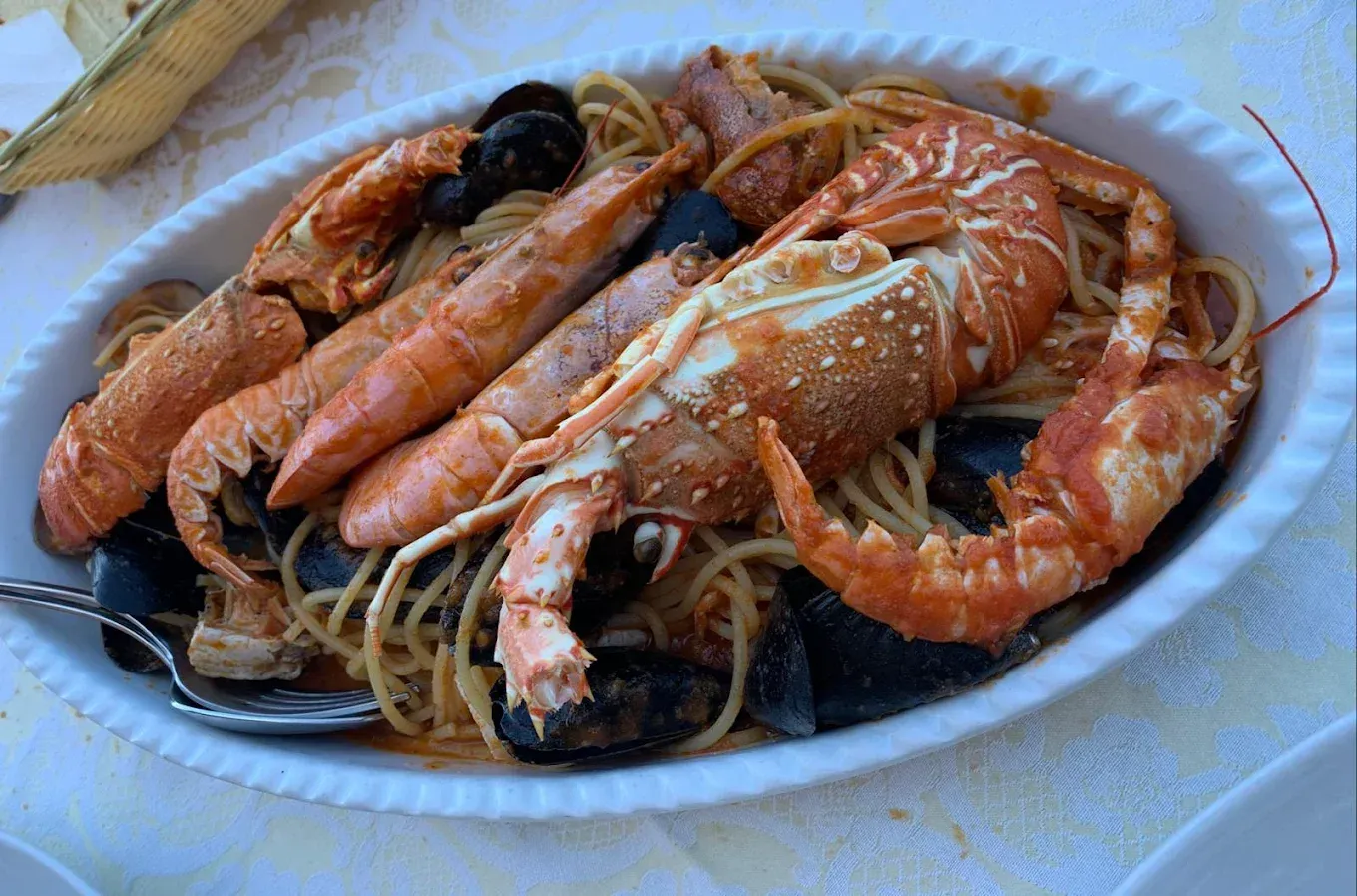 Un piatto bianco colmo di pasta ai frutti di mare con grossi scampi, gamberi e cozze in una salsa rossastra a base di pomodoro.