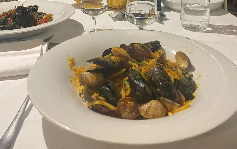 Primo piano di un piatto bianco colmo di pasta ai frutti di mare con cozze e vongole, adagiato su una tovaglia bianca.