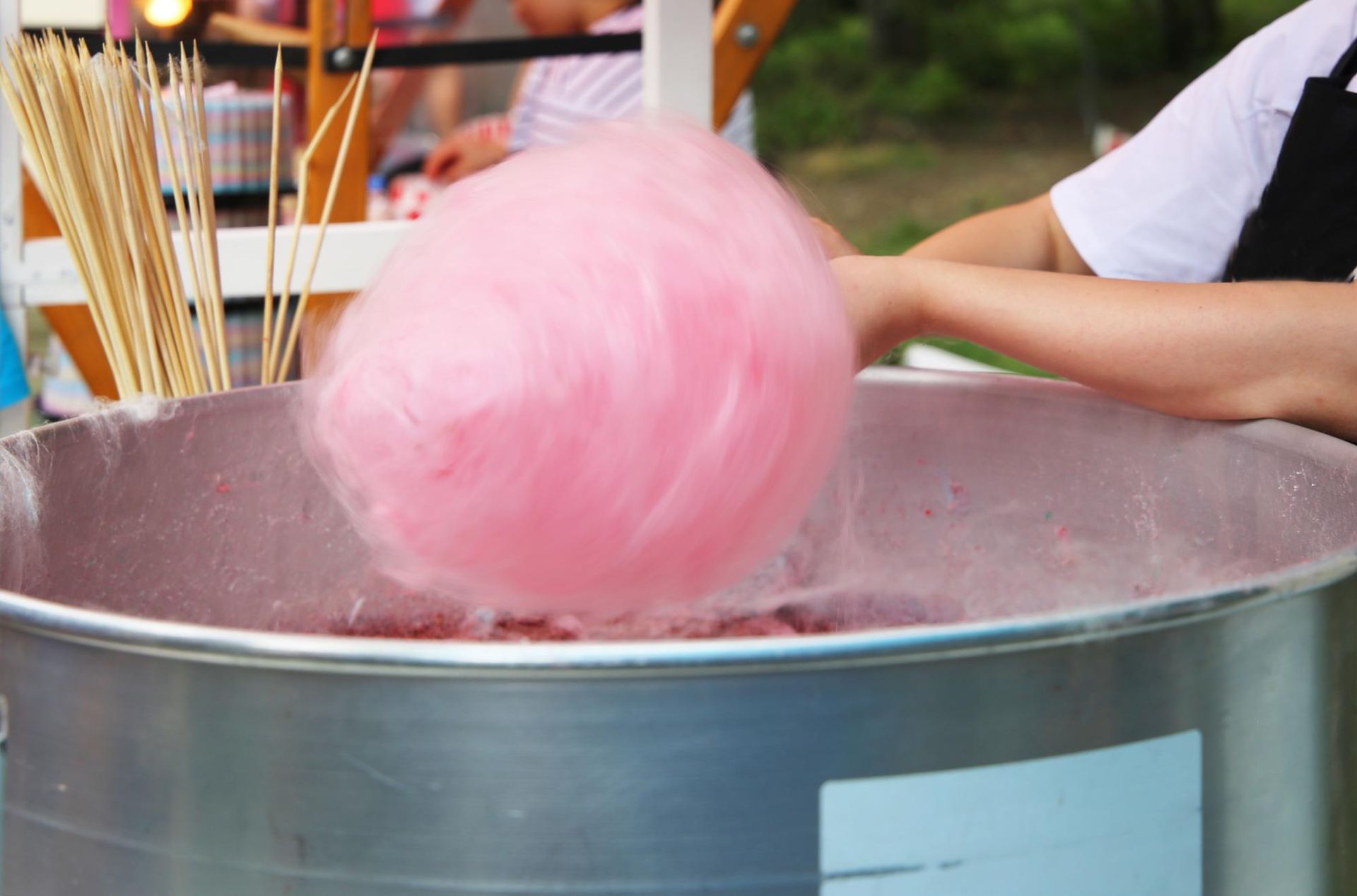 A person is making pink cotton candy in a large metal bowl.