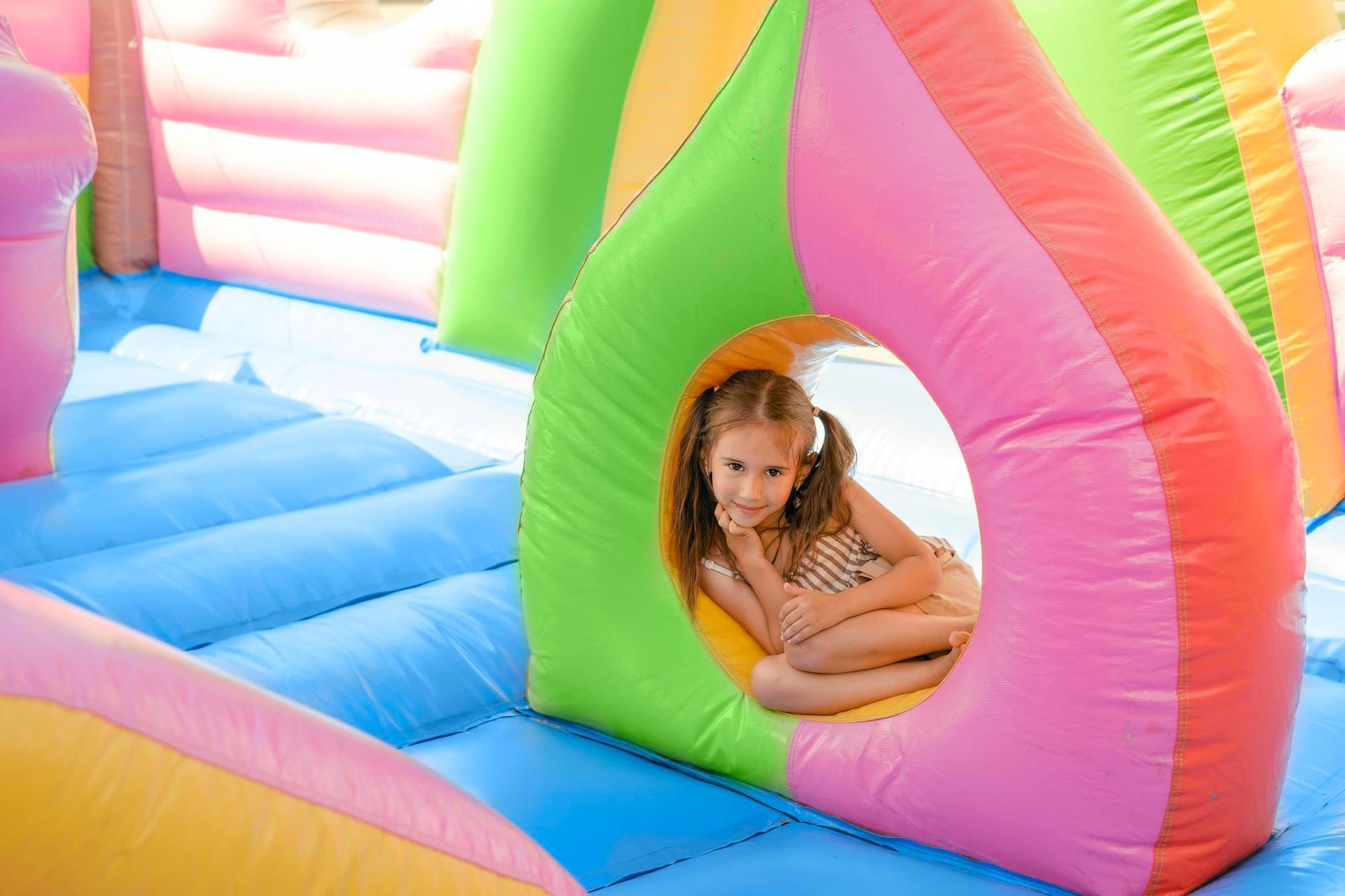 A little girl is sitting in a colorful inflatable house.