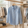 Camisa azul claro abotonada y pantalones beige colgados en percheros en una tienda de ropa.