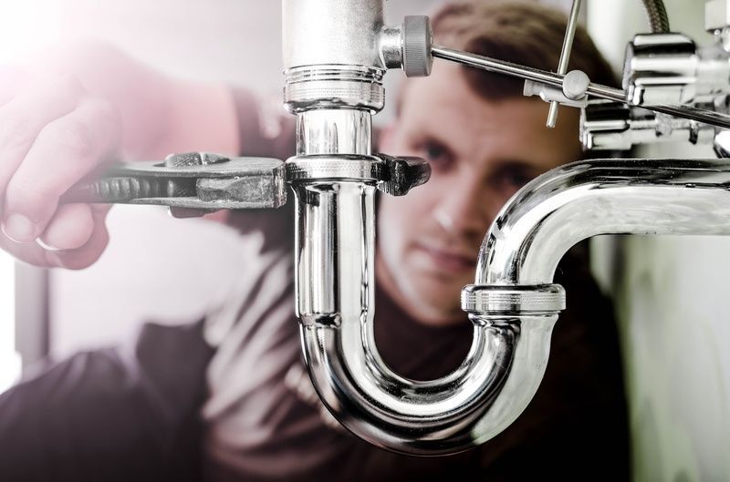 Brooks Plumbing Company plumber using a wrench on shiny chrome pipes; focused expression, indoor setting.