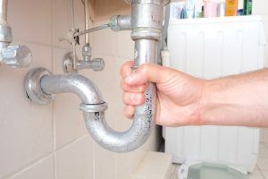 Hand holding a curved metal plumbing pipe under a sink.
