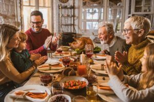 Family gathered around a table, clapping hands, ready to eat Thanksgiving dinner.