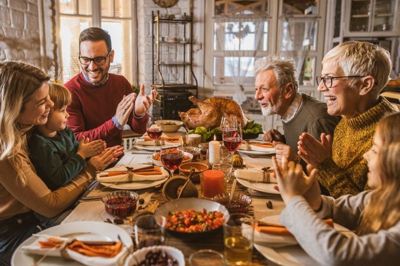 Family applauds around a Thanksgiving table with food, a turkey, and candles.