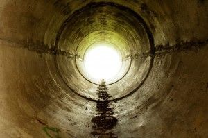 Inside of a concrete tunnel, bright light at the end.