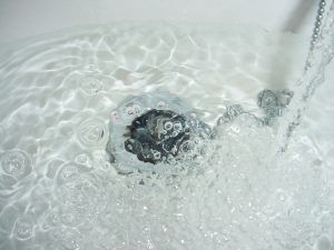 Water flowing into a white sink, with bubbles around the drain.