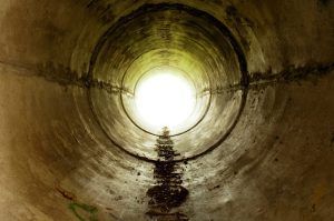 View from inside a dark concrete tunnel toward a bright, circular light.