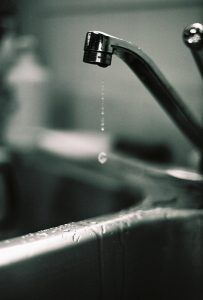 A dripping faucet over a stainless steel sink, black and white.