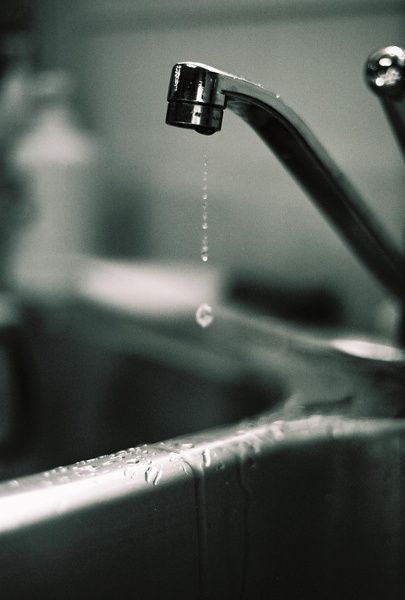 A silver faucet dripping water into a stainless steel sink.