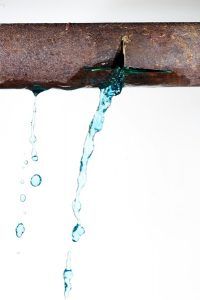 Rusty pipe with a leak, spraying blue liquid against a white background.