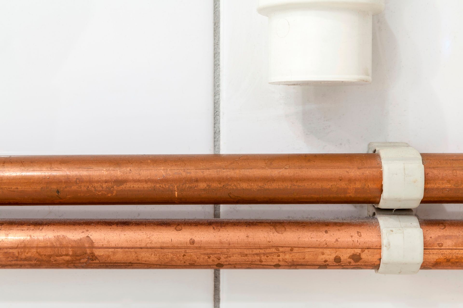 Copper pipes secured with white plastic clips on a white tiled wall.